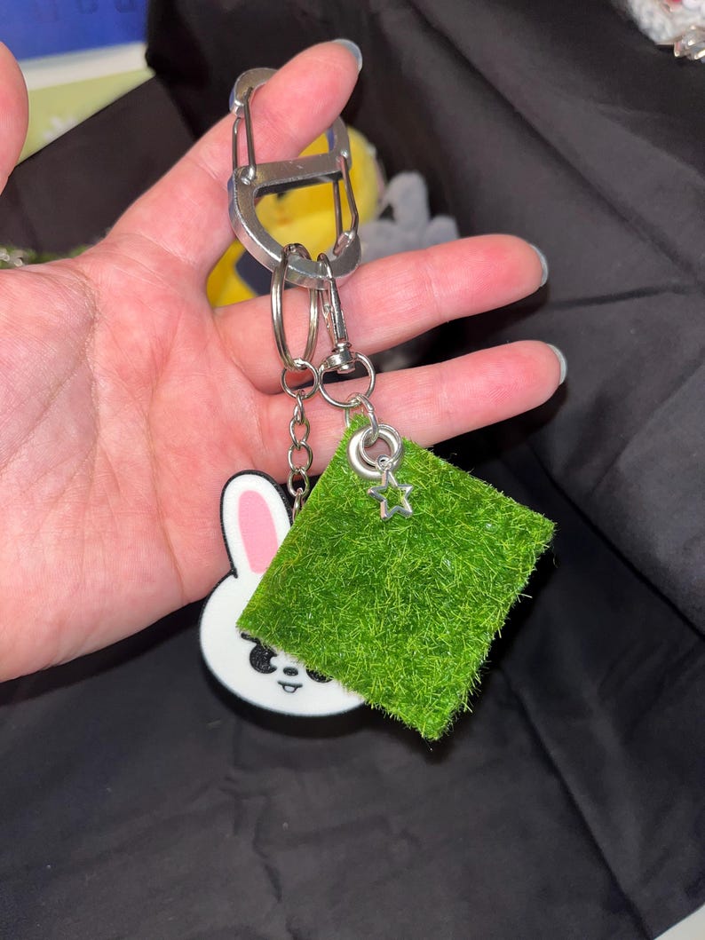 Puede incluir: Un llavero con un conejito blanco con orejas rosas y un cuadrado verde con un dije de estrella. El llavero est&aacute; sujeto a un mosquet&oacute;n y llaveros plateados.