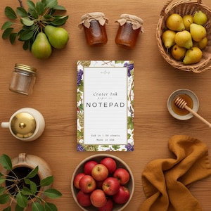 Könnte beinhalten: Ein rechteckiger Notizblock mit einem Weinreben-Rand, der den Text Crater Ink paper co. NOTEPAD und 5x8 in | 50 sheets Made in USA enthält. Der Notizblock ist umgeben von grünen Birnen, zwei kleinen Gläsern, einem Korb mit gelben Birnen, einem Honiglöffel und Äpfeln.