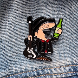 May include: A metal enamel pin featuring a cartoon character wearing a black hat and glasses, holding a black bass guitar in one hand and a green bottle in the other. The character has a grey goatee and wears a black coat over a red shirt.