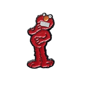 Puede incluir: Un pin de esmalte rojo con el personaje Elmo de Barrio Sésamo. El pin muestra a Elmo con un contorno negro, una nariz marrón, dientes blancos y una expresión pensativa. Es un artículo de colección.