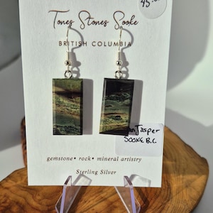 Puede incluir: Pendientes rectangulares con un diseño de piedra de jaspe verde y marrón, suspendidos de ganchos de plata de ley. La tarjeta del producto dice "Tones Stones Sooke, British Columbia" y "an Jasper Sooke B.C."