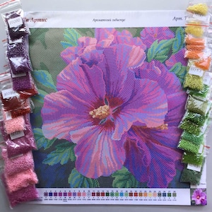 Peut inclure: Un kit de peinture diamant représentant une grande fleur d'hibiscus violette. Le kit comprend une toile avec le motif, des petits sachets de perles colorées et le texte "Ароматный гибискус".