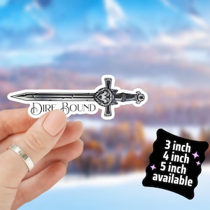 May include: A black and white sticker of a sword with the words "Dire Bound". The sword has a wolf head design on the hilt. Available in 3, 4, and 5 inch sizes.