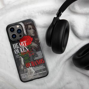 May include: Black phone case with the text "HEART QUEEN World Tour OURANOS" and a red rose graphic. The case features a woman's portrait and a list of song titles. Black over-ear headphones are also in the image.