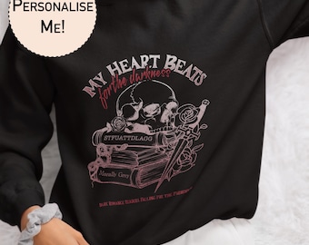 Peut inclure: Sweat-shirt noir avec un imprimé graphique rose d'un crâne, de livres et d'une dague. Le texte sur le graphique est "My heart beats for the darkness" et "Dark Romance Readers Falling for the Forbidden".