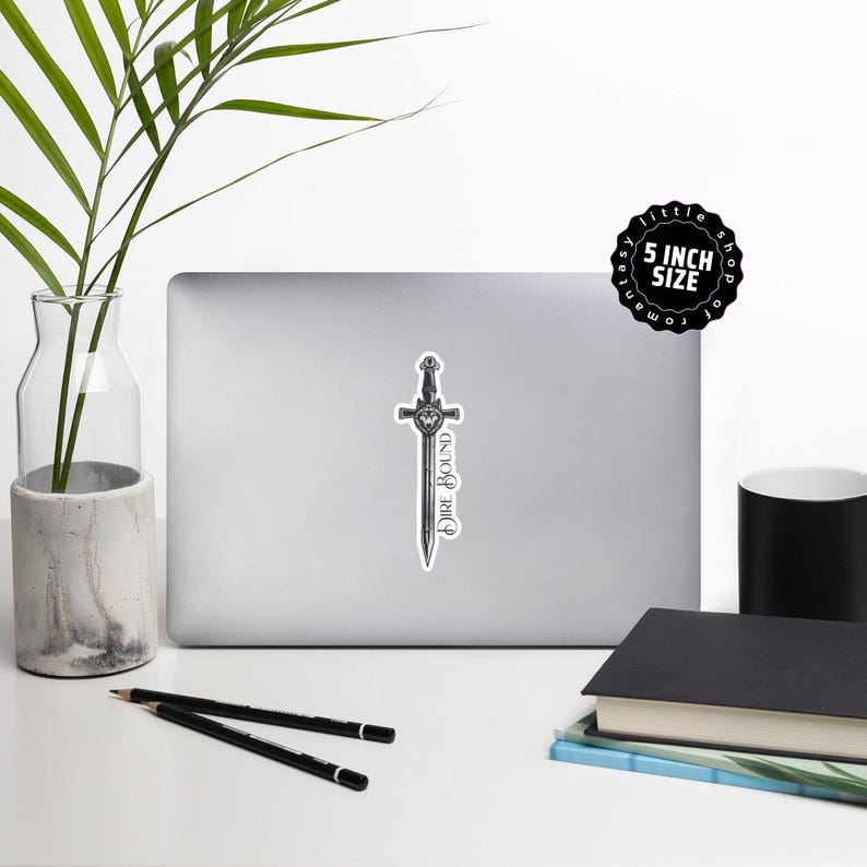 May include: A sticker featuring a detailed illustration of a sword with the words "Dire Bound" in a stylized font. The sticker is approximately 5 inches in size and is on a laptop.