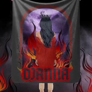 May include: A dark gray blanket featuring a graphic of a woman in a red dress and crown, surrounded by flames and a purple sky. The word "DJANNA" is displayed in red and black lettering. Text in red surrounds the central image.