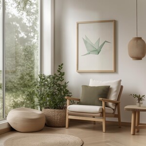 May include: A light wood armchair with a white cushion and a green throw pillow sits in a living room with a large window, a potted plant, and a framed print of a green origami crane.