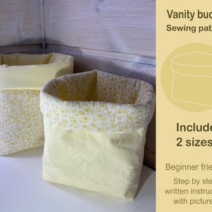 以下が含まれることがあります： 花柄の黄色い布製の収納バスケットが2つ。バスケットは柔らかくキルティングされた布地で作られています。画像には「Vanity bucket Sewing pattern Include 2 sizes Beginner friendly Step by step written instruction with pictures」というテキストが表示されています。
