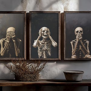 Puede incluir: Tres impresiones artísticas enmarcadas que representan esqueletos en las poses de 'No ver el mal, No oír el mal, No hablar el mal'. Cada impresión presenta un esqueleto sobre un fondo oscuro, con texto encima. Los marcos son de madera oscura y la obra de arte se exhibe en una estante de madera.