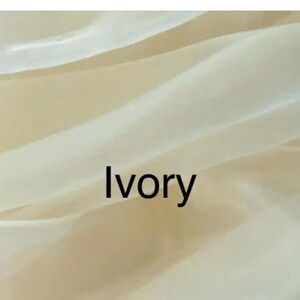 Op de afbeelding: Close-up van ivoorkleurige stof met zachte plooien en een doorschijnende kwaliteit. Het woord "Ivory" is zwart gedrukt, gecentreerd op de stof. De stof lijkt licht en vloeiend.