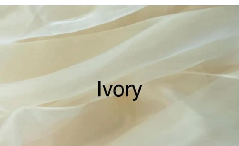 Op de afbeelding: Close-up van ivoorkleurige stof met zachte plooien en een doorschijnende kwaliteit. Het woord "Ivory" is zwart gedrukt, gecentreerd op de stof. De stof lijkt licht en vloeiend.