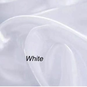 Op de afbeelding: Close-up van witte stof met zachte plooien. Het woord "White" is in het zwart onderaan de afbeelding gedrukt. De stof lijkt doorschijnend en vloeiend, met highlights en schaduwen die diepte cre&euml;ren.