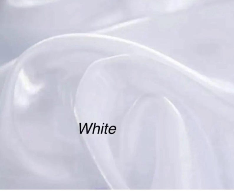 Op de afbeelding: Close-up van witte stof met zachte plooien. Het woord "White" is in het zwart onderaan de afbeelding gedrukt. De stof lijkt doorschijnend en vloeiend, met highlights en schaduwen die diepte cre&euml;ren.