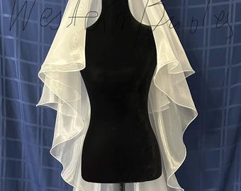 May include: A white, layered bridal veil displayed on a black mannequin. The veil has a soft, flowing appearance with multiple tiers. The background is a blue fabric with a grid pattern.