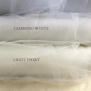 Puede incluir: Primer plano de cuatro tonos diferentes de tela de tul: blanco, blanco diamante, marfil claro e marfil. Los nombres de los colores est&aacute;n impresos encima de cada muestra. El tul tiene un tejido fino y abierto.