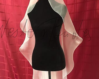 May include: A sheer, light pink bridal veil with a wavy edge is draped over a black mannequin. The veil is made of a delicate, translucent fabric. The mannequin is on a black stand against a red backdrop.