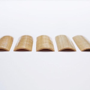 Puede incluir: Cinco cañas de oboe de madera de diferentes tamaños, dispuestas en fila sobre una superficie blanca.