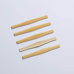 Pode incluir: Cinco palhetas de madeira de cor clara são dispostas diagonalmente sobre uma superfície branca. Cada palheta tem uma seção central ligeiramente mais larga e extremidades afiladas. As palhetas parecem novas e não utilizadas, com grão de madeira natural.