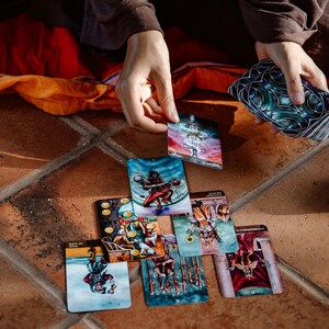 May include: A collection of tarot cards with colorful illustrations, including images of figures, symbols, and scenes. The cards are arranged on a terracotta tile surface, with hands holding and selecting cards from the deck. The cards have a mystical theme.