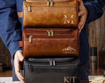 May include: Three rectangular toiletry bags stacked vertically. The top bag is light brown with the name MICHAEL and an M monogram. The middle bag is dark brown with a mountain graphic and the name LAWRENCE. The bottom bag is black with the initials K|T.
