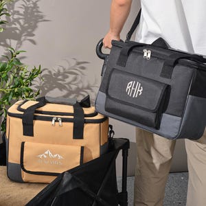 May include: Two insulated cooler bags. One is tan with black accents and a mountain logo with the name "Benjamin". The other is black and gray with a monogram. Both have top handles and shoulder straps.