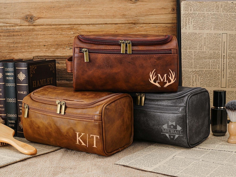 May include: Three brown leather wash bags with zip closures and gold-coloured hardware. One bag has the initials "KT", another has the letter "M" with antlers, and the third has the name "MICHAEL".