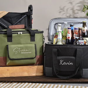 May include: Two insulated cooler bags, one olive green and one black, sit side-by-side. The green cooler has "Steven Groomsman" embroidered on the front. The black cooler has "Kevin" embroidered on the front. Both are open, revealing bottles of beer.