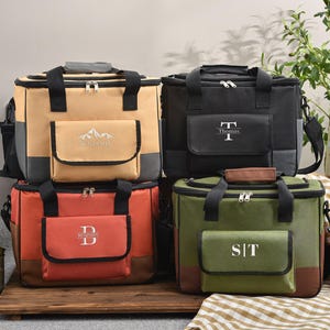 以下が含まれることがあります： ベージュ、黒、赤、緑の4つのパーソナライズされたクーラーバッグ。各バッグには、モノグラムまたは名前が付いたフロントポケットが付いています。バッグには黒いハンドル、ジッパー、ショルダーストラップが付いています。ベージュのバッグには山のデザインがあります。