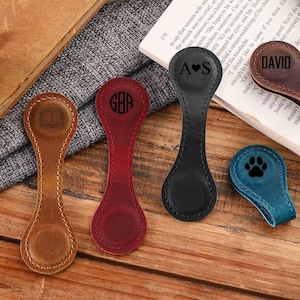 May include: Five different leather book magnets with various designs. The magnets are brown, black, red, blue, and teal. The designs include a book, a heart with the letters AS, the letters GAB, the word DAVID, and a paw print.