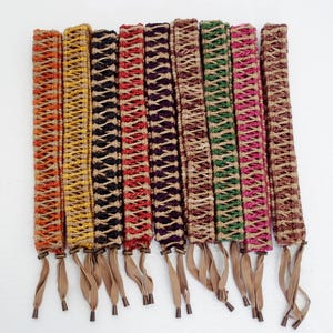 May include: Assortment of ten colourful woven trims with fringe ends. The trims are made of natural fibres and have a variety of patterns and colours, including red, orange, yellow, green, blue, and purple.
