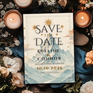 May include: Save the Date card with a mountain range illustration in blue and white, with gold stars and text. The text reads "Save the Date", "Adeline & Connor", "Are Getting Married", and "10.10.2025". The card is surrounded by flowers and candles.