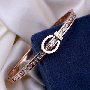 May include: A rose gold bangle bracelet with a clear crystal encrusted band and a circular clasp with the word "LOVE" engraved on it.