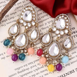 May include: A pair of gold-tone dangle earrings with clear teardrop-shaped crystals and colorful beads. The earrings have a traditional Indian design.