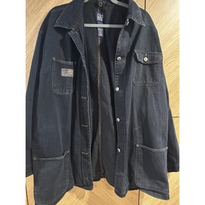 May include: A dark blue denim jacket with a button-up front, collar, and multiple pockets. The jacket has a relaxed fit and features the "GAP" logo on the back of the collar. The jacket has a vintage look.