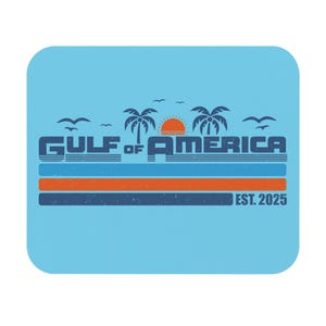 May include: A light blue mousepad with a retro design. The design features the text "GULF OF AMERICA" in blue, with palm trees, a setting sun, and the text "EST. 2025". Below the text are two horizontal stripes in orange and blue.