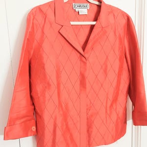 May include: A coral-colored long-sleeve jacket featuring a diamond-stitched quilted pattern throughout the front. The jacket has a notched collar, a button-front closure, and cuffs with a single button. A label reads CARLISLE at the neck.
