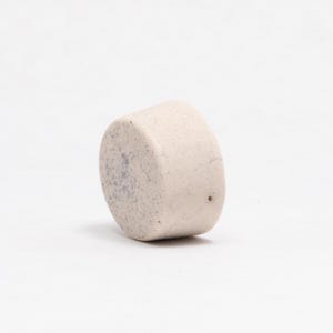 Op de afbeelding: Een kleine, ronde, witte keramische pot met een gespikkelde textuur. De pot heeft een klein gaatje in de bodem voor drainage.