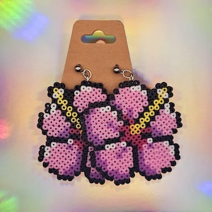 May include: A pair of pink and yellow flower-shaped earrings made of perler beads. The earrings are attached to silver hooks.