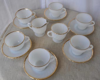 May include: A collection of white teacups and saucers with gold trim. The set includes several teacups, saucers, and a creamer. The cups and saucers have a delicate, vintage appearance, perfect for serving tea or coffee.