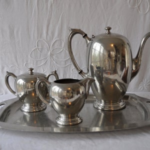 May include: A silver tea set on a silver tray. The set includes a teapot, creamer, and sugar bowl.