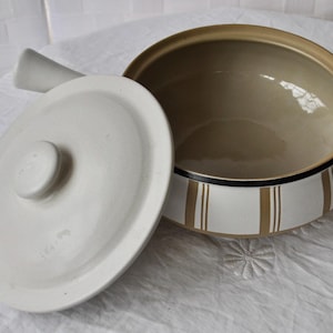 May include: A white ceramic casserole dish with a brown and white striped design. The dish has a lid with a knob on top.