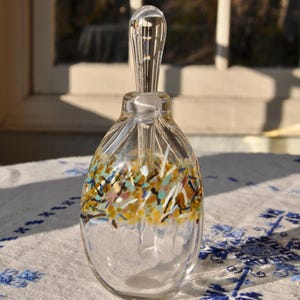 May include: A clear glass bottle with a textured surface and a colorful, confetti-like design around the middle. The bottle has a clear glass stopper.