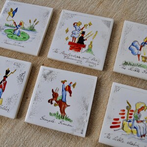 May include: Set of six square ceramic tiles with hand-painted illustrations of fairy tale scenes. Each tile features a different image with text, including "Thumbelina," "The Shepherdess and the Chimney Sweeps," and "The Little Swineherd."