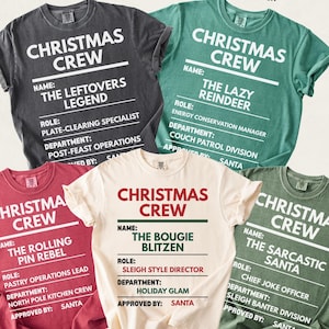 Set of Comfort Colors unisex Christmas T-shirts in festive tones: Pepper, Light Green, Crimson, Ivory, and Moss. Each shirt reads “CHRISTMAS CREW” at the top with a fun holiday badge layout showing “NAME,” “ROLE,” and “DEPARTMENT.” Designs include The Leftovers Legend, The Lazy Reindeer, The Rolling Pin Rebel, The Bougie Blitzen, and The Sarcastic Santa, each with humorous holiday titles and North Pole–themed departments.