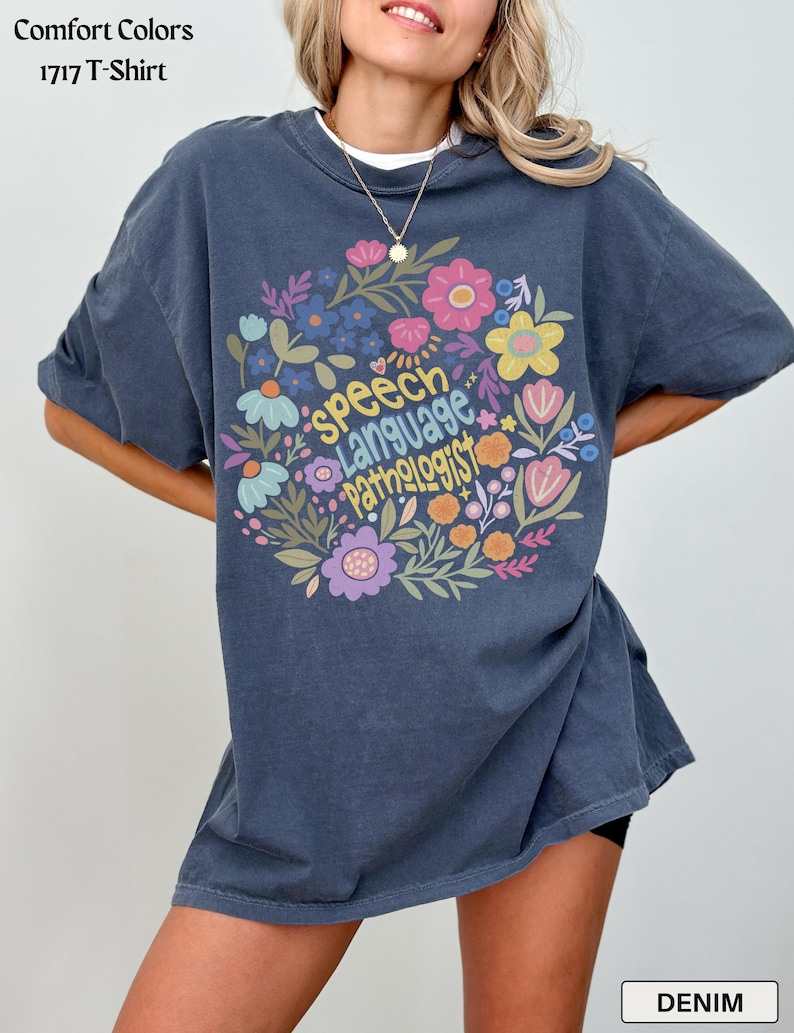 Puede incluir: Camiseta Comfort Colors 1717 azul denim con un dise&ntilde;o floral y las palabras "Speech Language Pathologist". El dise&ntilde;o incluye flores rosas, amarillas, azules y moradas. La camiseta es de corte holgado.