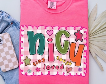 May include: A bright pink t-shirt with the word "NICU" in colorful letters, surrounded by hearts, stars, and the words "tiny, tough, loved." The shirt has a gingham pattern and the text "CRUNCHBERRY" at the bottom.