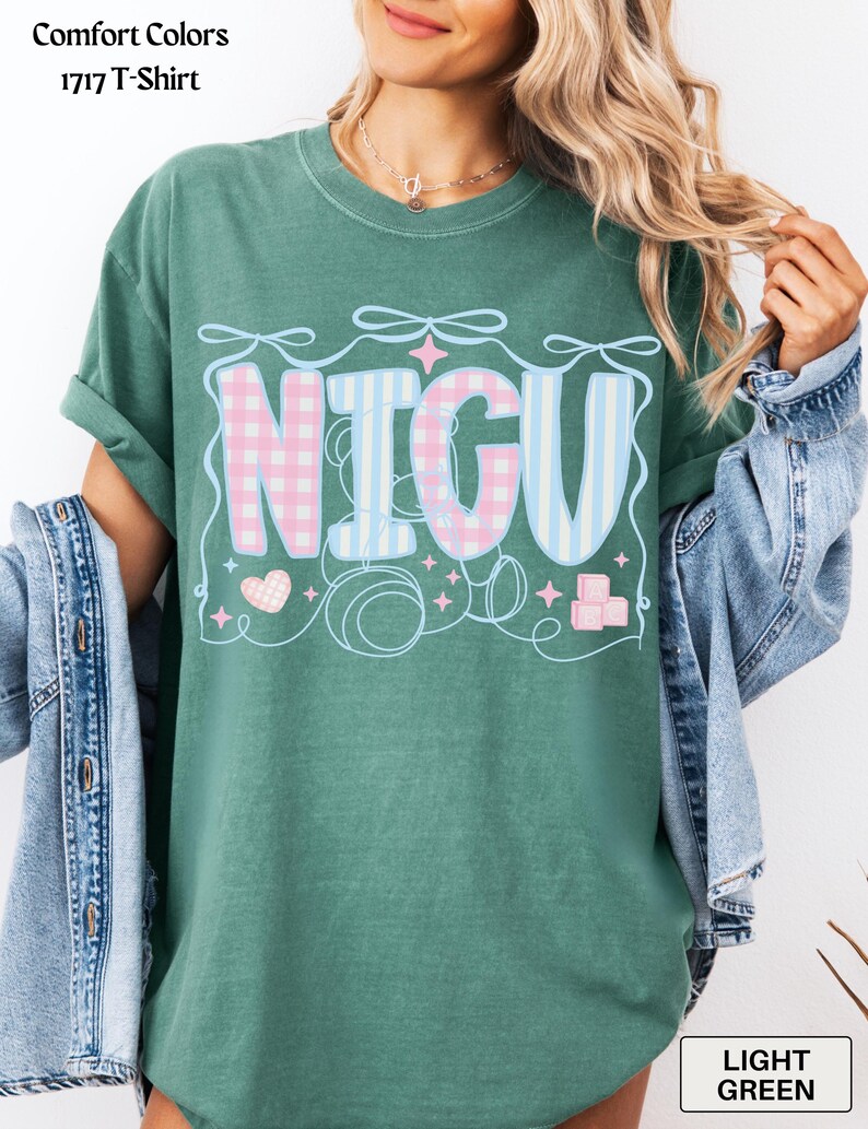 May include: A light green t-shirt with the word "NICU" in pink and blue checkered and striped patterns. The word is surrounded by decorative elements including hearts, stars, and bows.