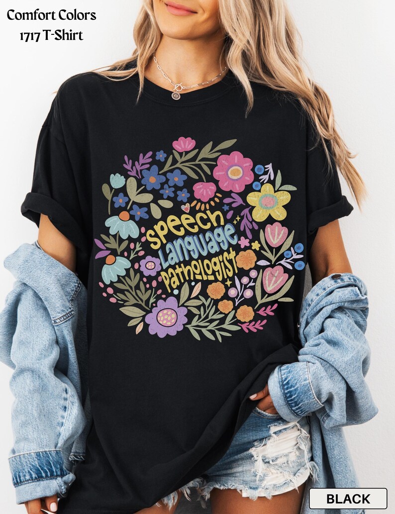 Puede incluir: Camiseta negra con un dise&ntilde;o floral que rodea las palabras "Speech Language Pathologist" en amarillo. El arreglo floral incluye flores rosas, azules, moradas y amarillas. La camiseta es una Comfort Colors 1717 T-Shirt.