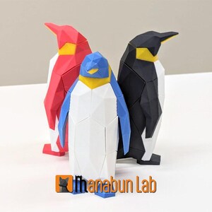 May include: Three origami penguins, one red, one black, and one white with blue wings. The penguins are standing on a white surface.
